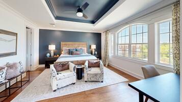 A bedroom with a large bed, two armchairs, a small table, and a view of the outside through large windows.