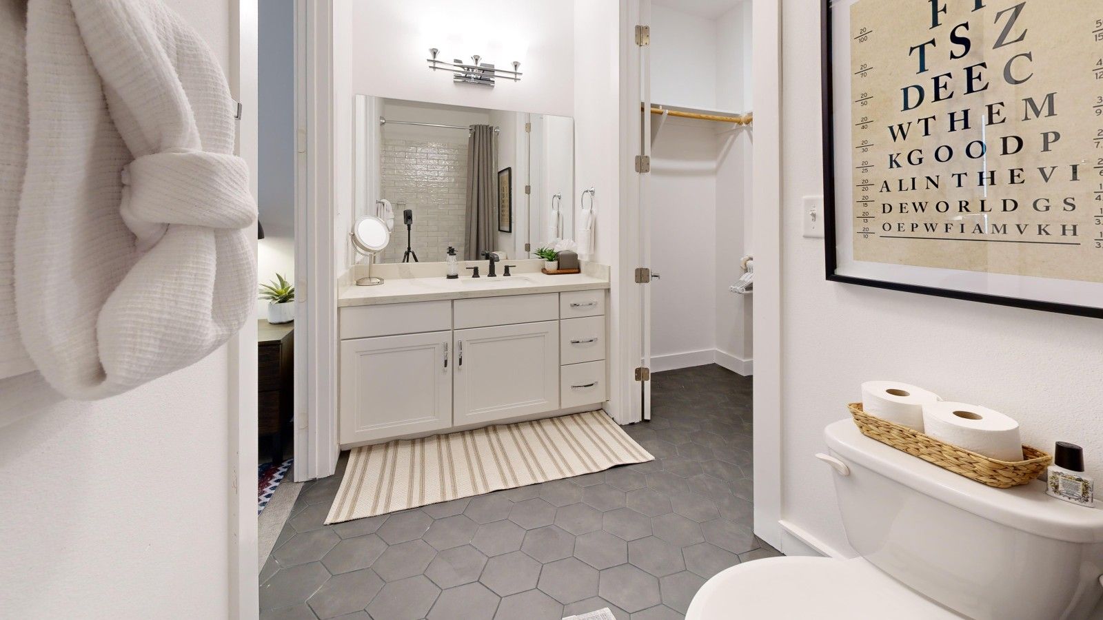 Une salle de bain avec un meuble-lavabo blanc, un miroir, un porte-serviettes et des toilettes avec du papier toilette.