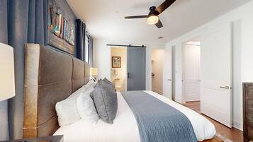 A bedroom with a large bed, a ceiling fan, and a door leading to another room.