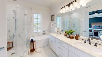 A modern bathroom with a glass shower enclosure, a bathtub, a vanity with a large mirror, and a window providing natural light.