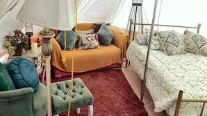 Ein Zeltraum mit einer Couch, einem Bett, einem Sessel und einer Lampe.