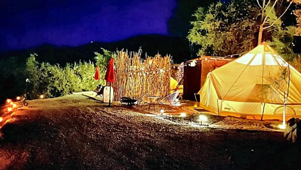 Ein Zelt auf schottrigem Untergrund, mit einem roten Sonnenschirm und Campingstühlen in der Nähe.