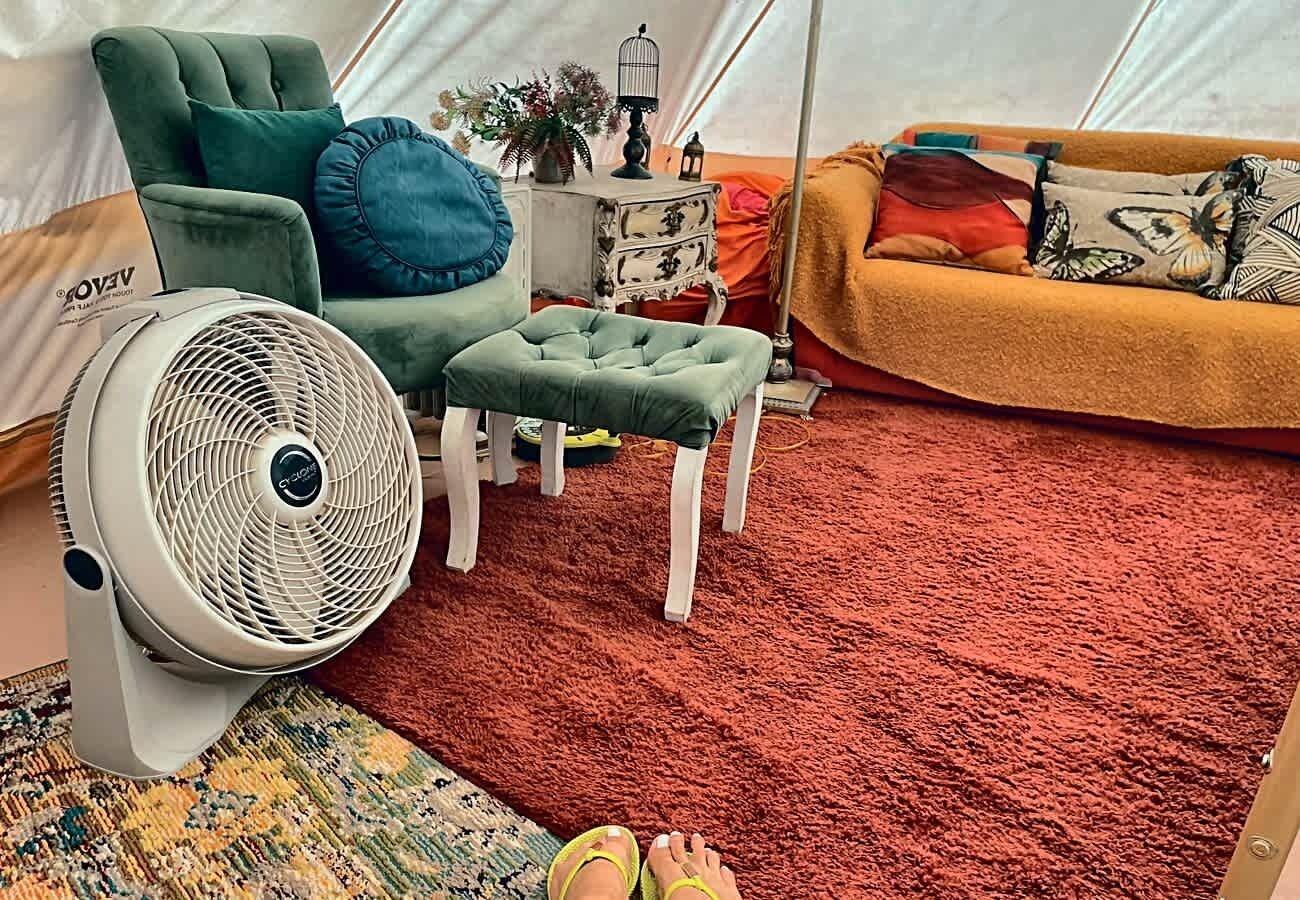 Ein Zeltinnenraum mit Sofa, Hocker, Ventilator und einem gemusterten Teppich.