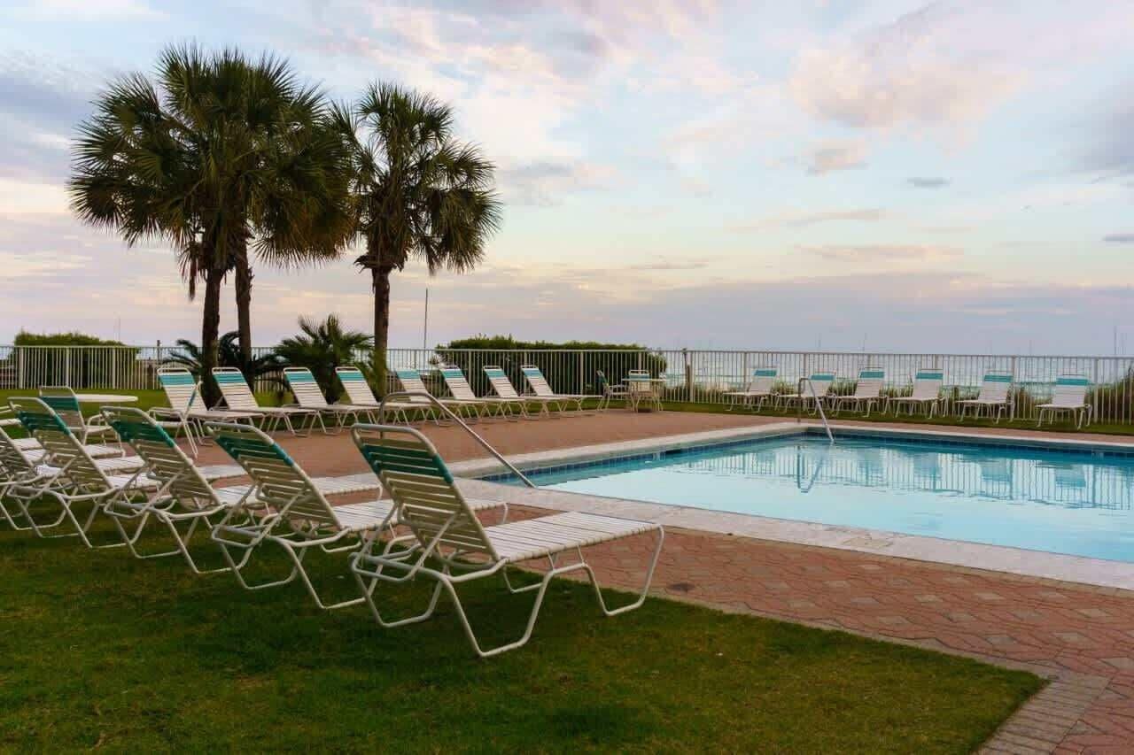 Un área de piscina con sillones de descanso y palmeras.