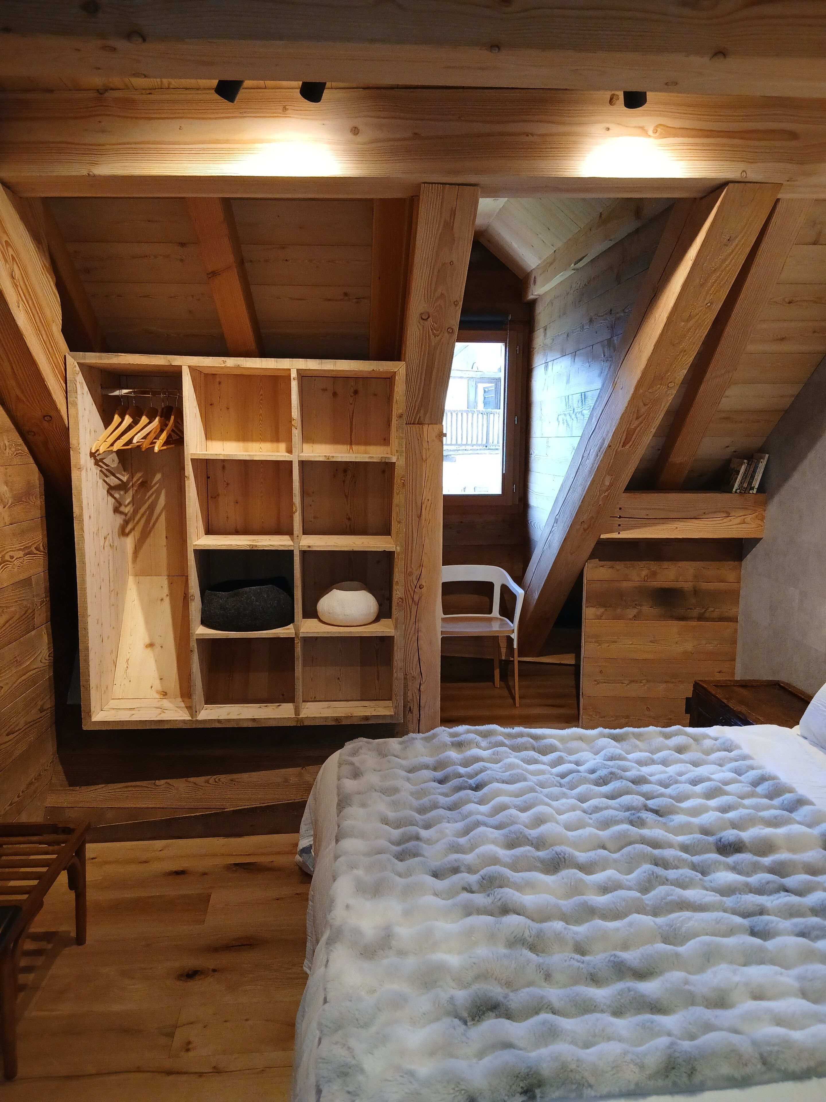 A wooden attic bedroom with a bed, a built-in shelf unit, and a window.