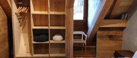 Une chambre mansardée en bois, avec un lit, une bibliothèque intégrée et une fenêtre.