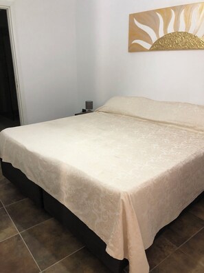 Un lit avec une couvre-lit à motifs, une table de chevet avec une lampe et un mur orné d’un élément décoratif.