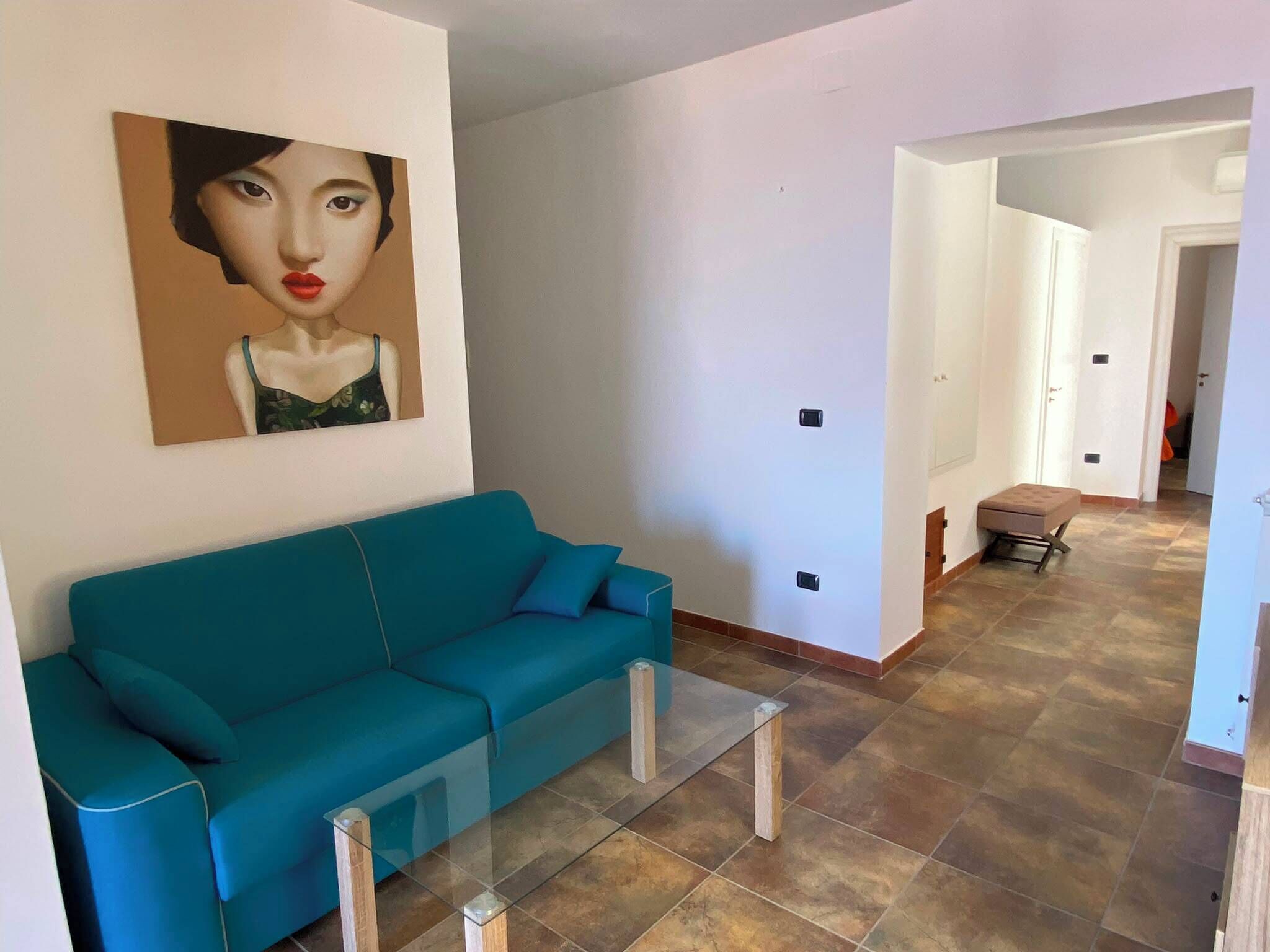 A living room with a teal sofa, a glass coffee table, and a painting on the wall.