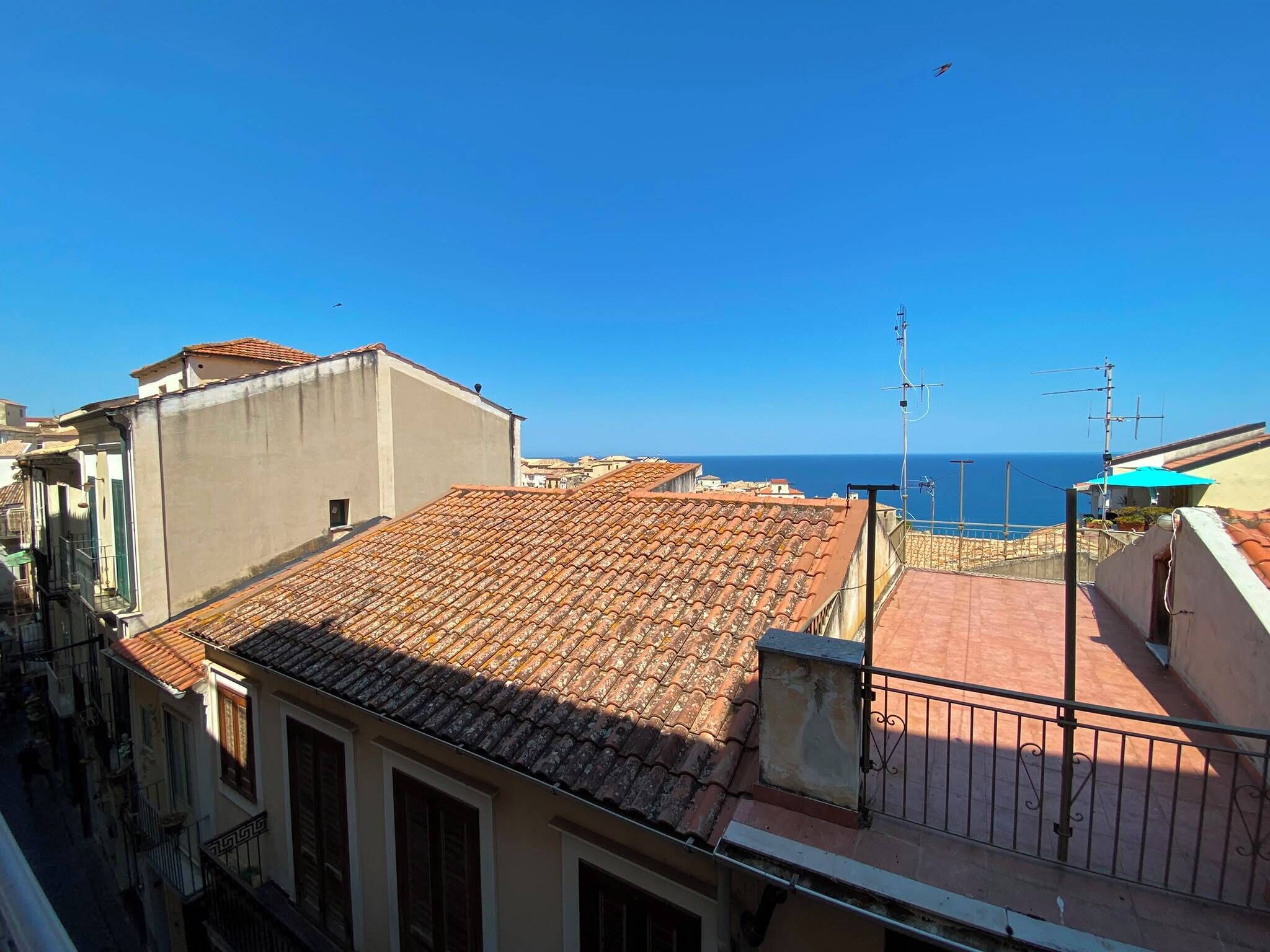 Ein Küstenwohngebiet mit terrakottafarbenen Dächern, blauem Himmel und Blick aufs Meer.