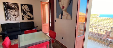 A living room with a black sofa, red chairs, a glass-top table, and two framed portraits on the wall.