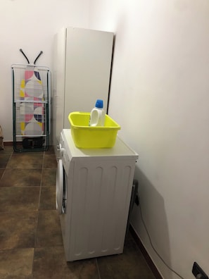 A laundry area with a washing machine, a yellow basin on top, and a drying rack with patterned cloth. - Charming vacation rental in the heart of the historic center of Pizzo, Calabria (Pizzo)