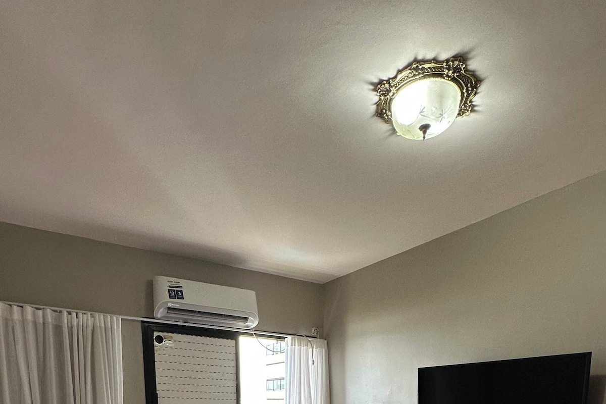 Hotelkamer met een bed, bureau, flatscreen-tv aan de muur, airconditioning boven het raam en uitzicht op het omliggende landschap.