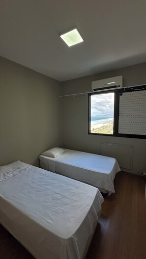 Een kamer met twee bedden, een raam met uitzicht op het strand en een airconditioning.