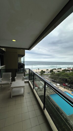 Een balkon met uitzicht op de oceaan, een zwembad en terrasmeubilair.