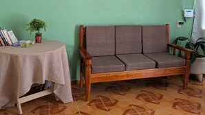 A room with a green wall, a wooden sofa, a round table with a tablecloth, and a potted plant.