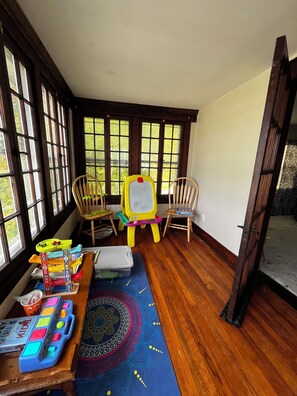 A room with large windows, a wooden floor, a children's play area with a chalkboard, and a patterned rug. - CatalpaCorner 2-Bed Peace-filled/Sunroom/Turnkey/Mid-term/Monthly/Weekly (Springfield)