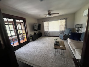 A living room with a ceiling fan, a television, a sofa, a coffee table, and a window with curtains.
