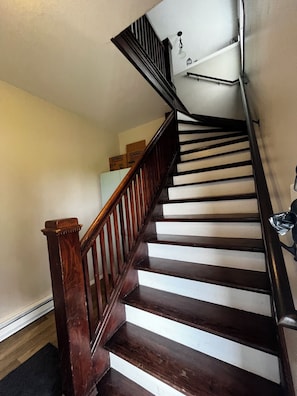 A wooden staircase with white risers and a black handrail, leading to a landing with a light fixture. - CatalpaCorner 2-Bed Peace-filled/Sunroom/Turnkey/Mid-term/Monthly/Weekly (Springfield)