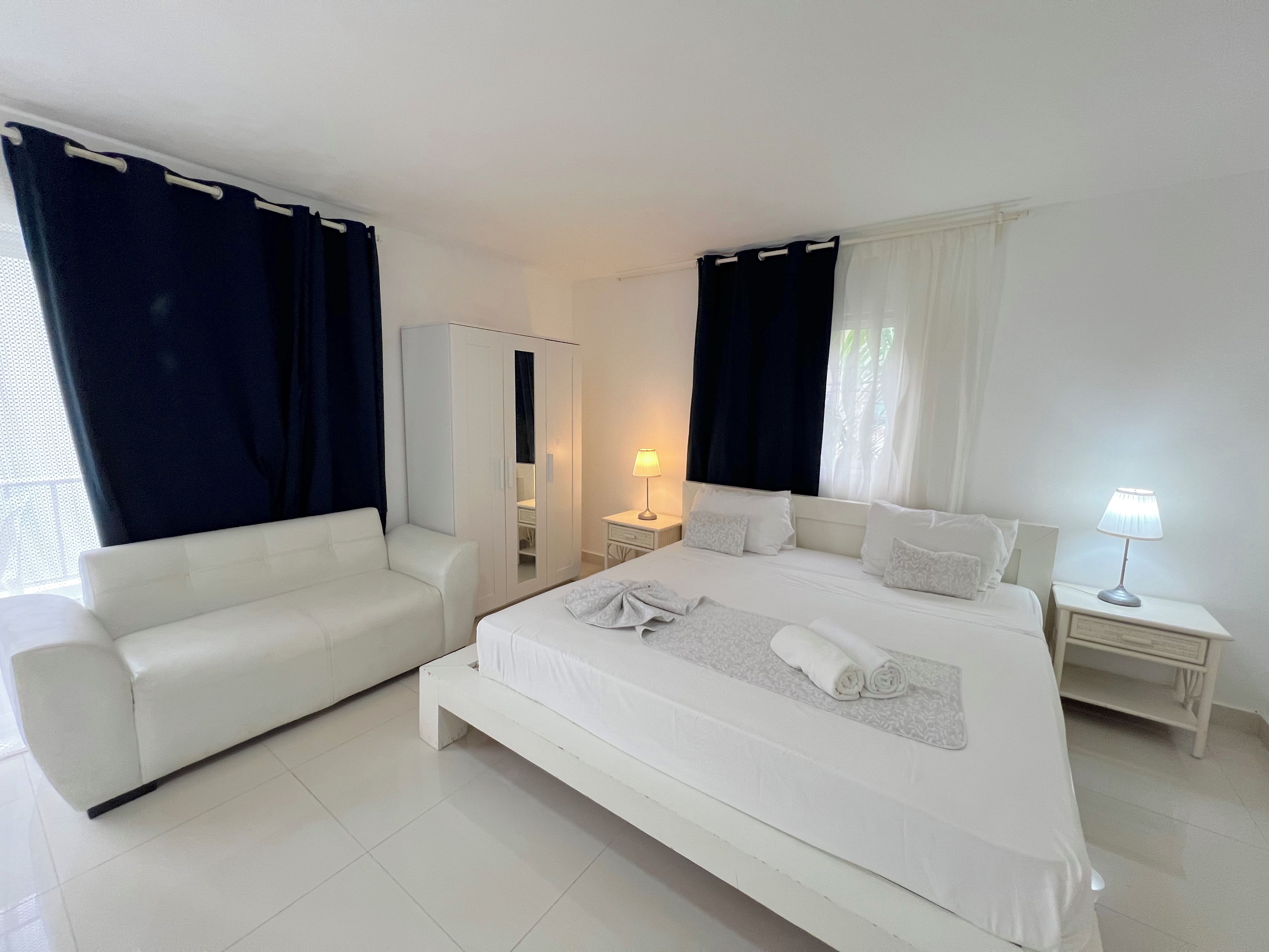 Una habitación de hotel con cama, sofá, armario, mesita de noche y lámpara.