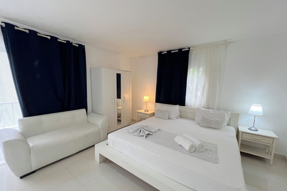 A hotel room with a bed, a sofa, a wardrobe, a nightstand, and a lamp.