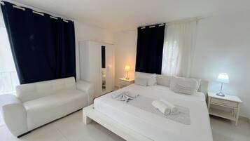 Una habitación de hotel con cama, sofá, armario, mesita de noche y lámpara.