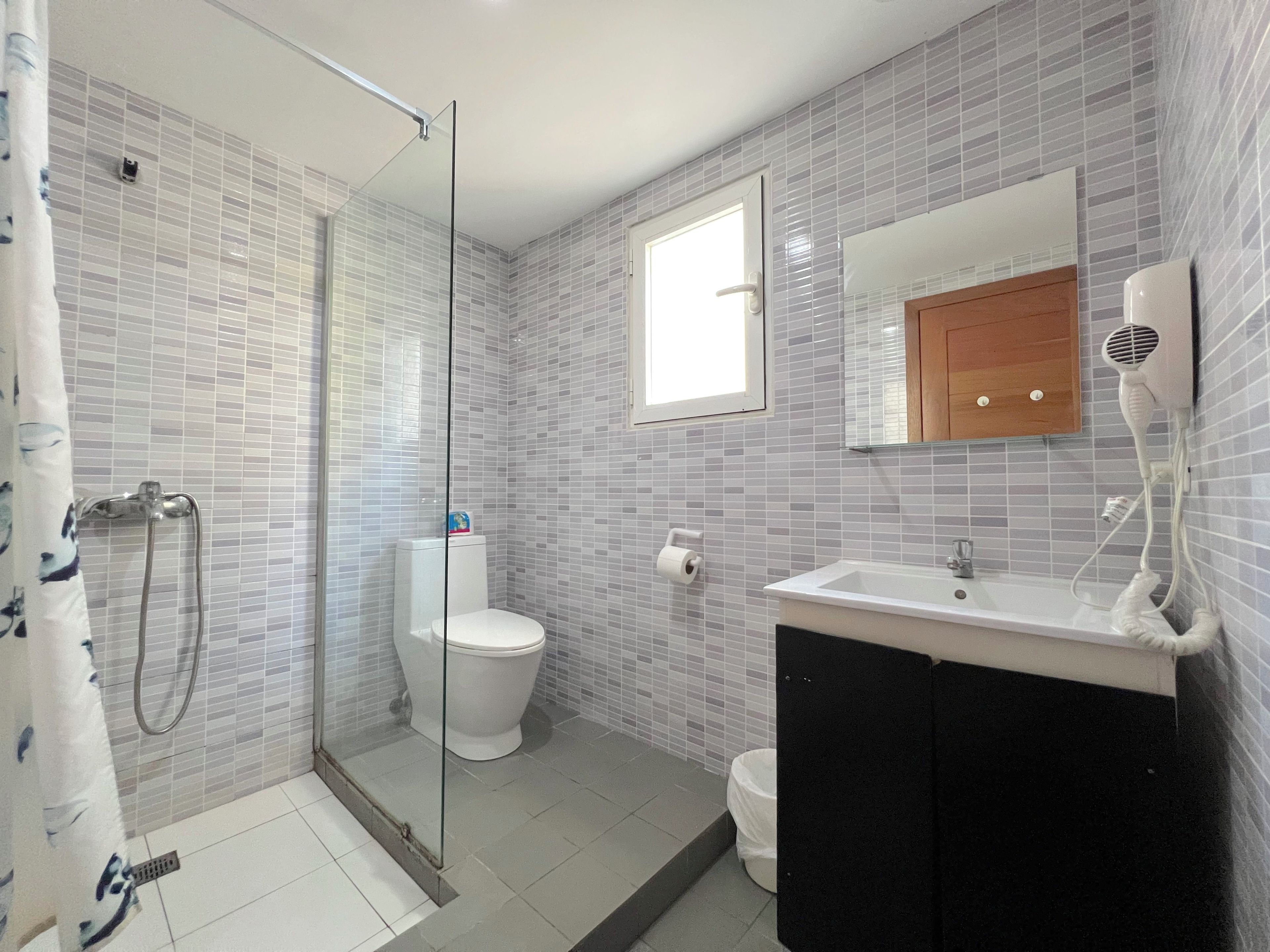 Un baño con cabina de ducha de vidrio, inodoro, lavabo con espejo y toallero.