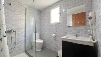 Un baño con cabina de ducha de vidrio, inodoro, lavabo con espejo y toallero.