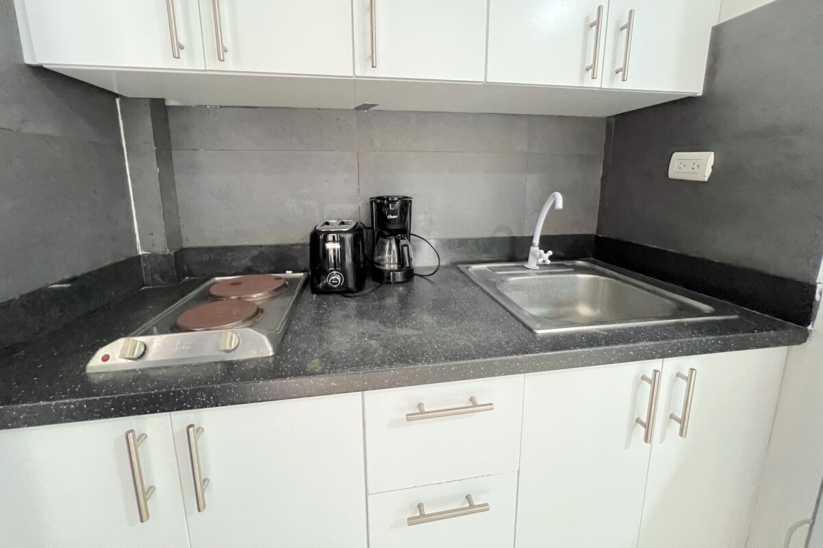 A kitchen with white cabinets, a black countertop, a coffee maker, a toaster, and a sink.