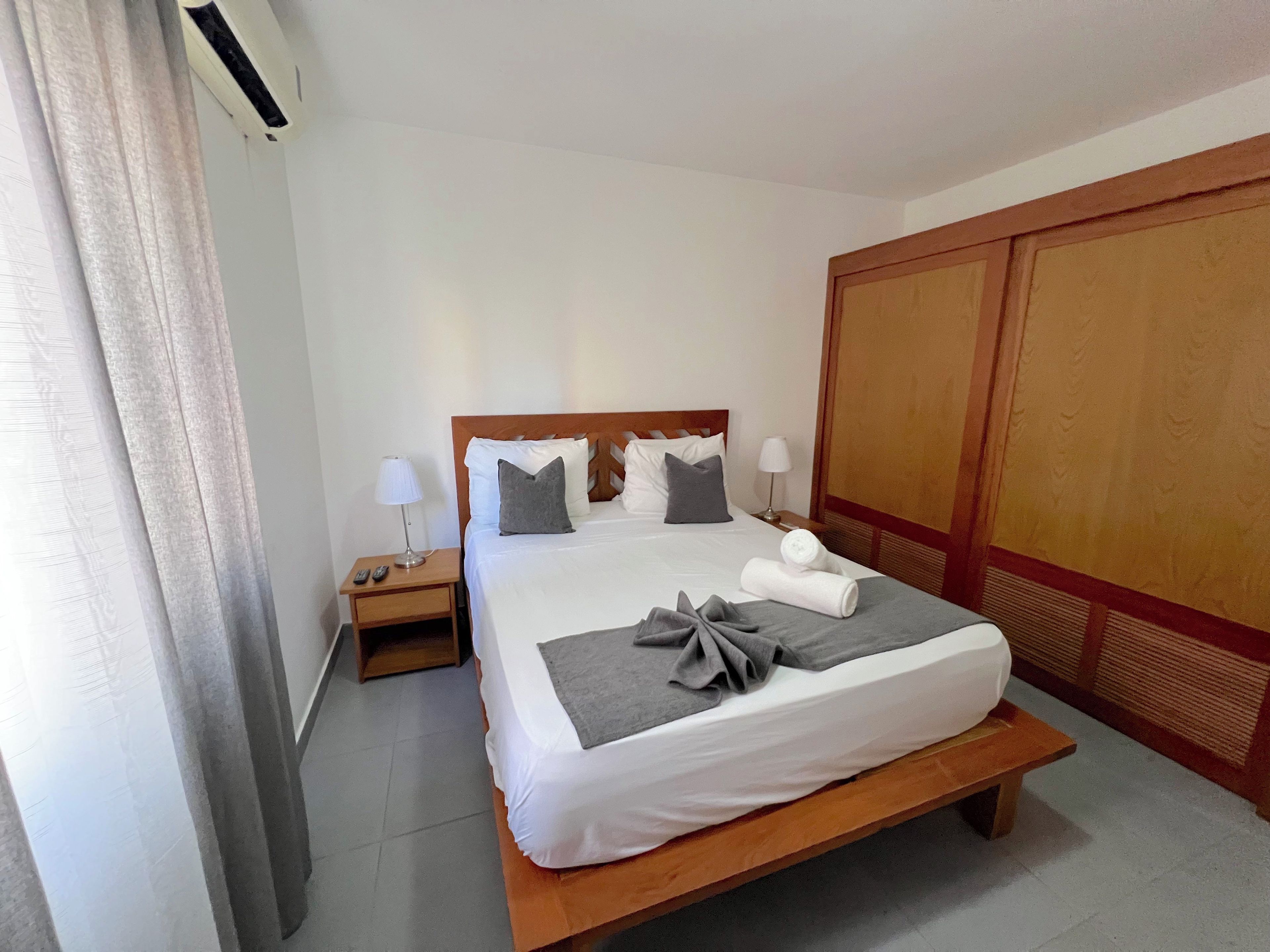 A hotel room with a single bed, bedside tables, a wardrobe, and an air conditioning unit.