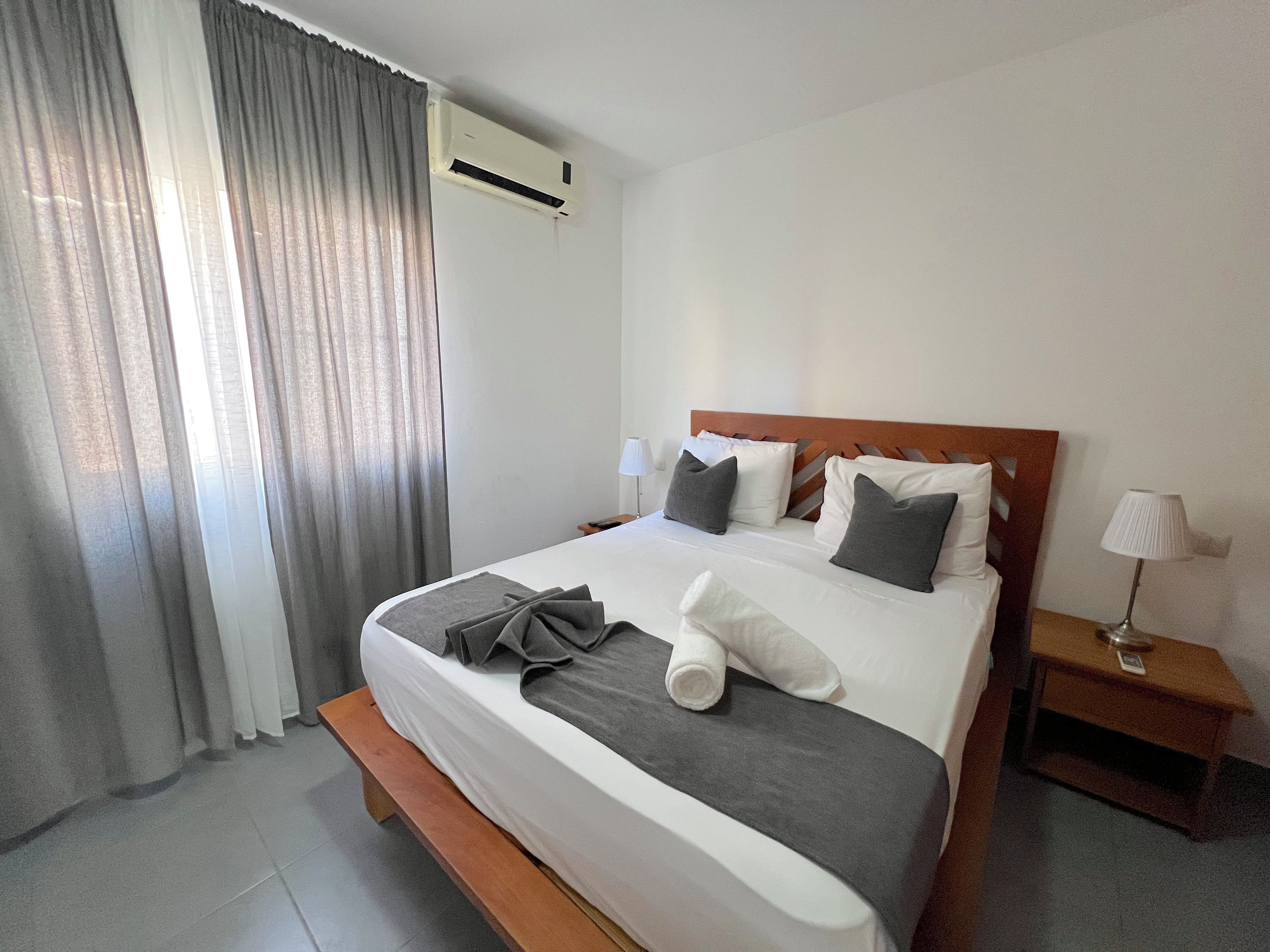 Habitación de hotel con una cama, una mesita de noche, una lámpara y un ventanal con cortinas.