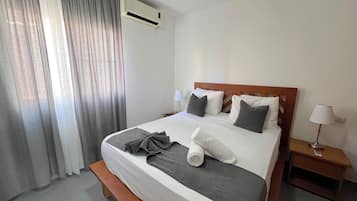 Habitación de hotel con una cama, una mesita de noche, una lámpara y un ventanal con cortinas.