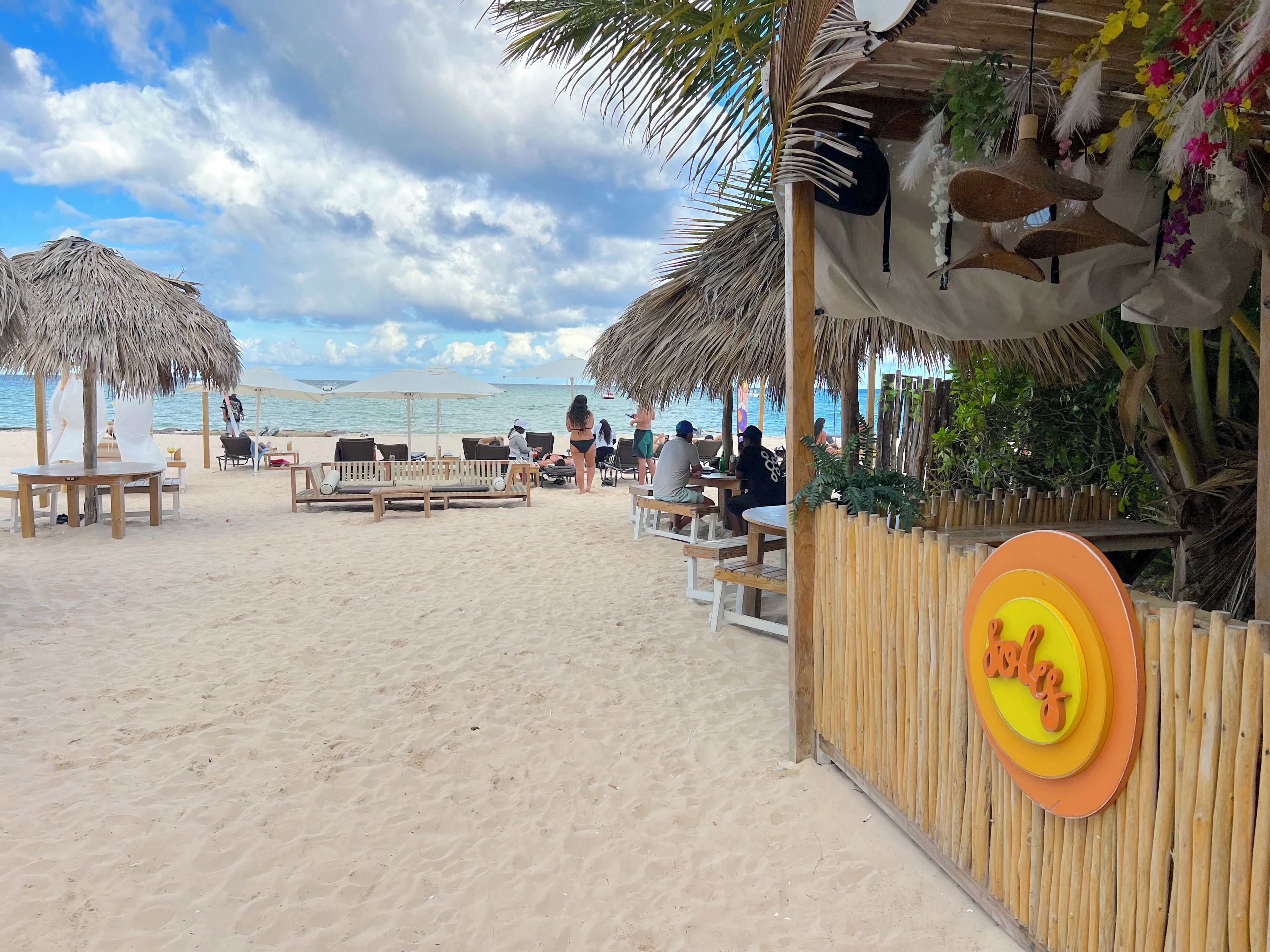 Ein Restaurant am Strand mit Außenbestuhlung, einem Reetdach und einem Holzzaun.
