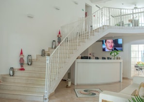 Un vaste espace de vie avec un escalier menant à un niveau supérieur, un téléviseur à écran plat fixé au mur et une plante décorative au niveau inférieur.