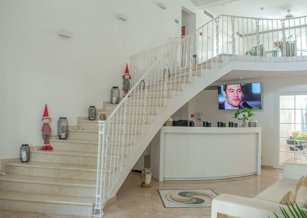 A spacious living area with a staircase leading to an upper level, a flat-screen TV mounted on the wall, and a decorative plant on the lower level.