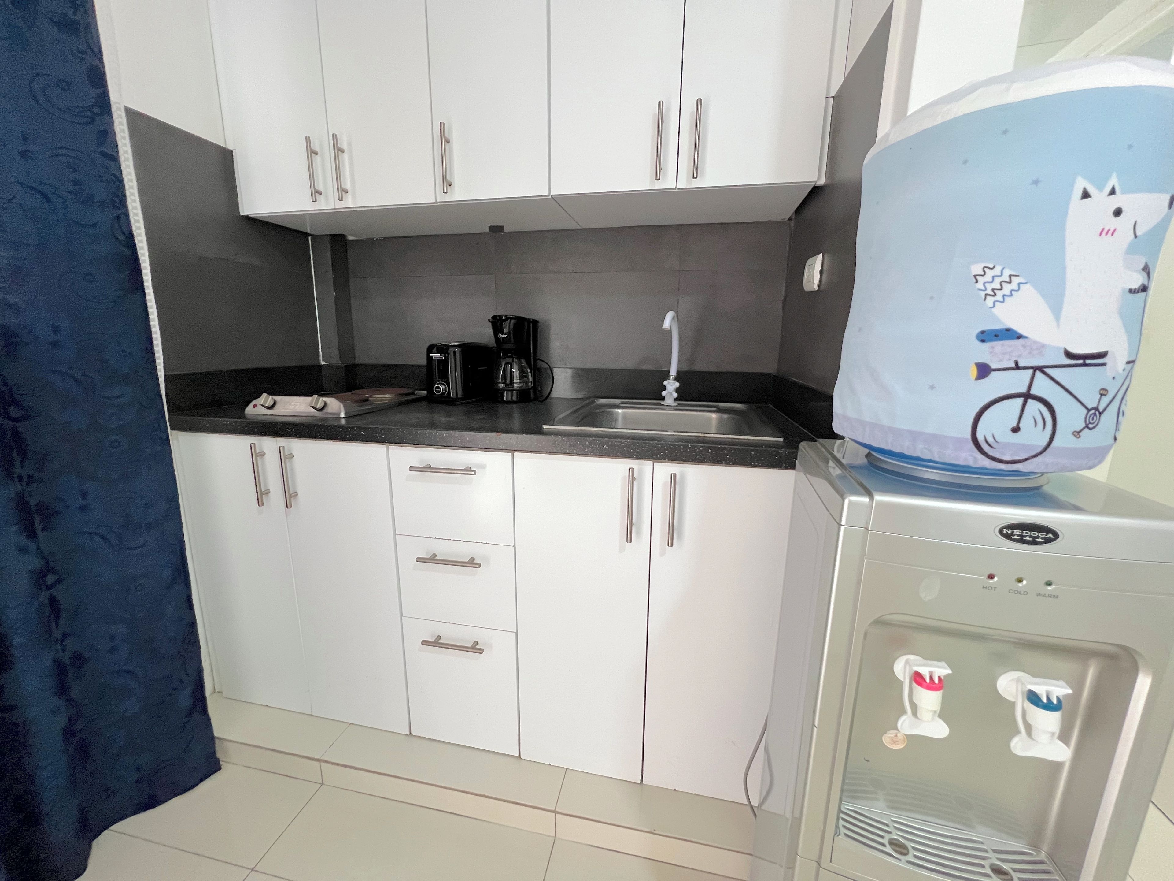 A kitchen with white cabinets, a coffee maker, a water dispenser, and a refrigerator.
