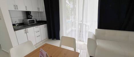 A compact living space with a kitchenette, a dining table with a sign, and a sofa.