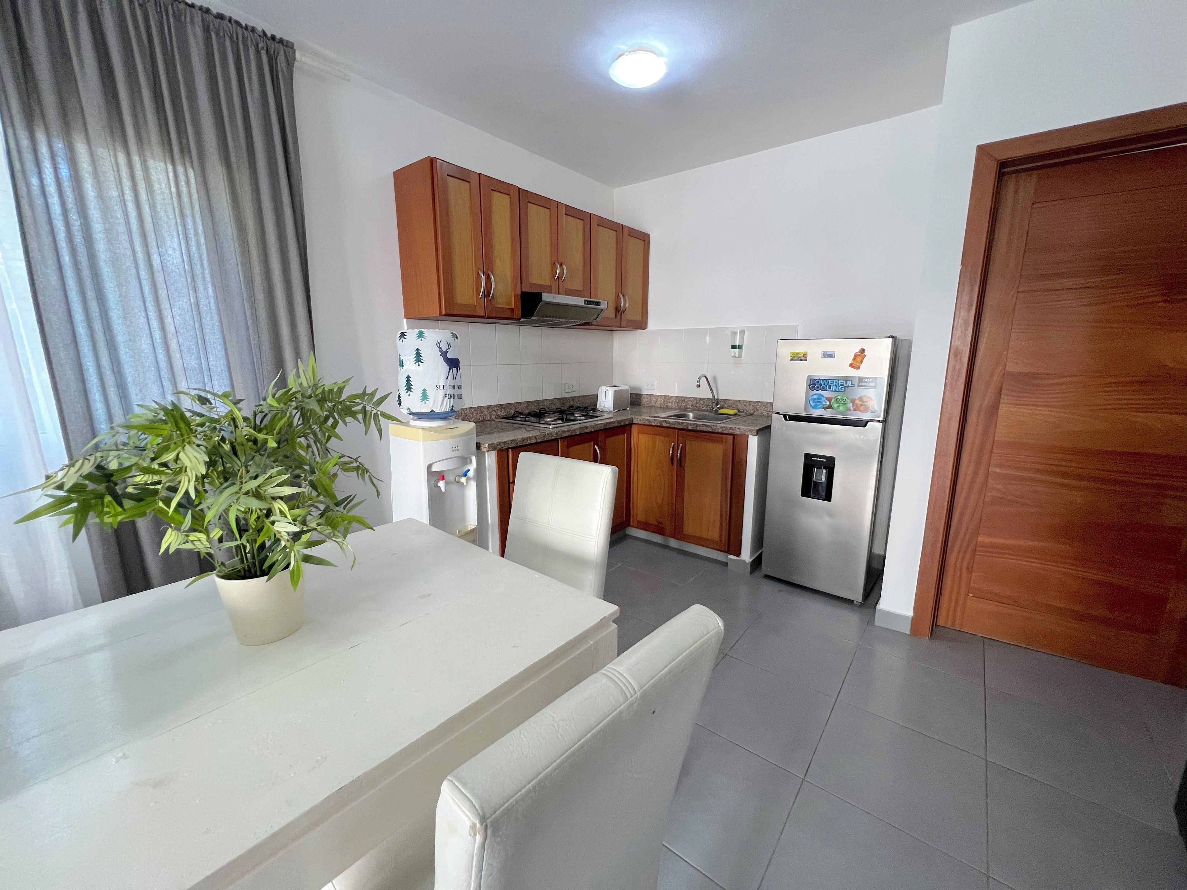 Una cocina compacta con muebles de madera, un refrigerador, un dispensador de agua y una mesa de comedor con sillas.
