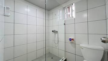 Ein Badezimmer mit weißen Fliesen, einer Glasduschkabine, einer Toilette und einem kleinen Fenster.