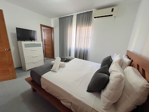 A hotel room with a bed, a TV on a dresser, a door, and an air conditioning unit.
