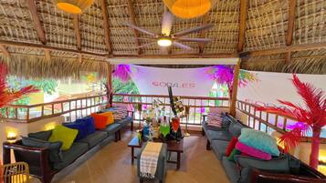 A spacious room with a thatched ceiling, multiple seating areas, and a central table with various items.