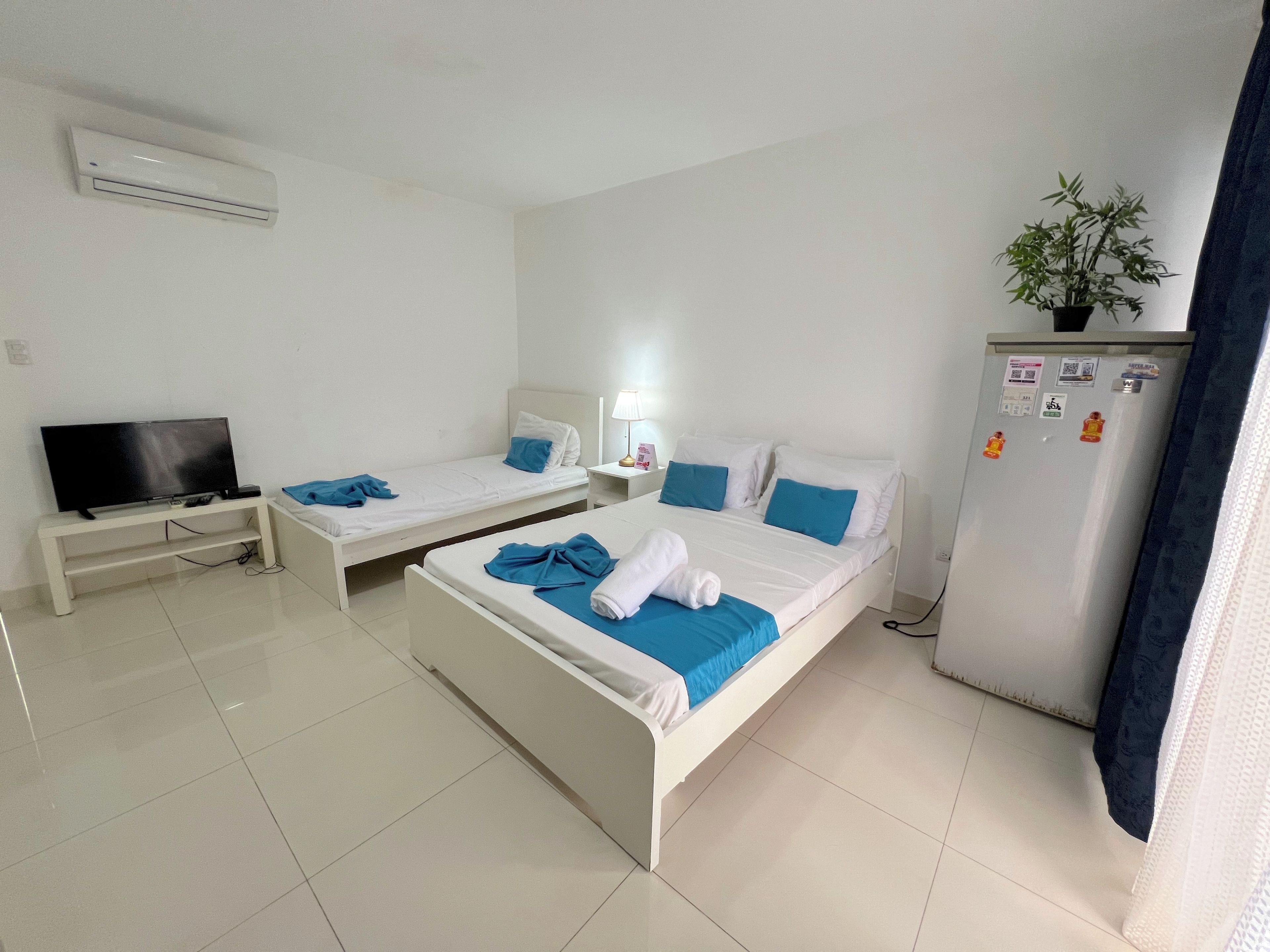 Una habitación de hotel con dos camas, un televisor, un refrigerador y una planta en maceta.