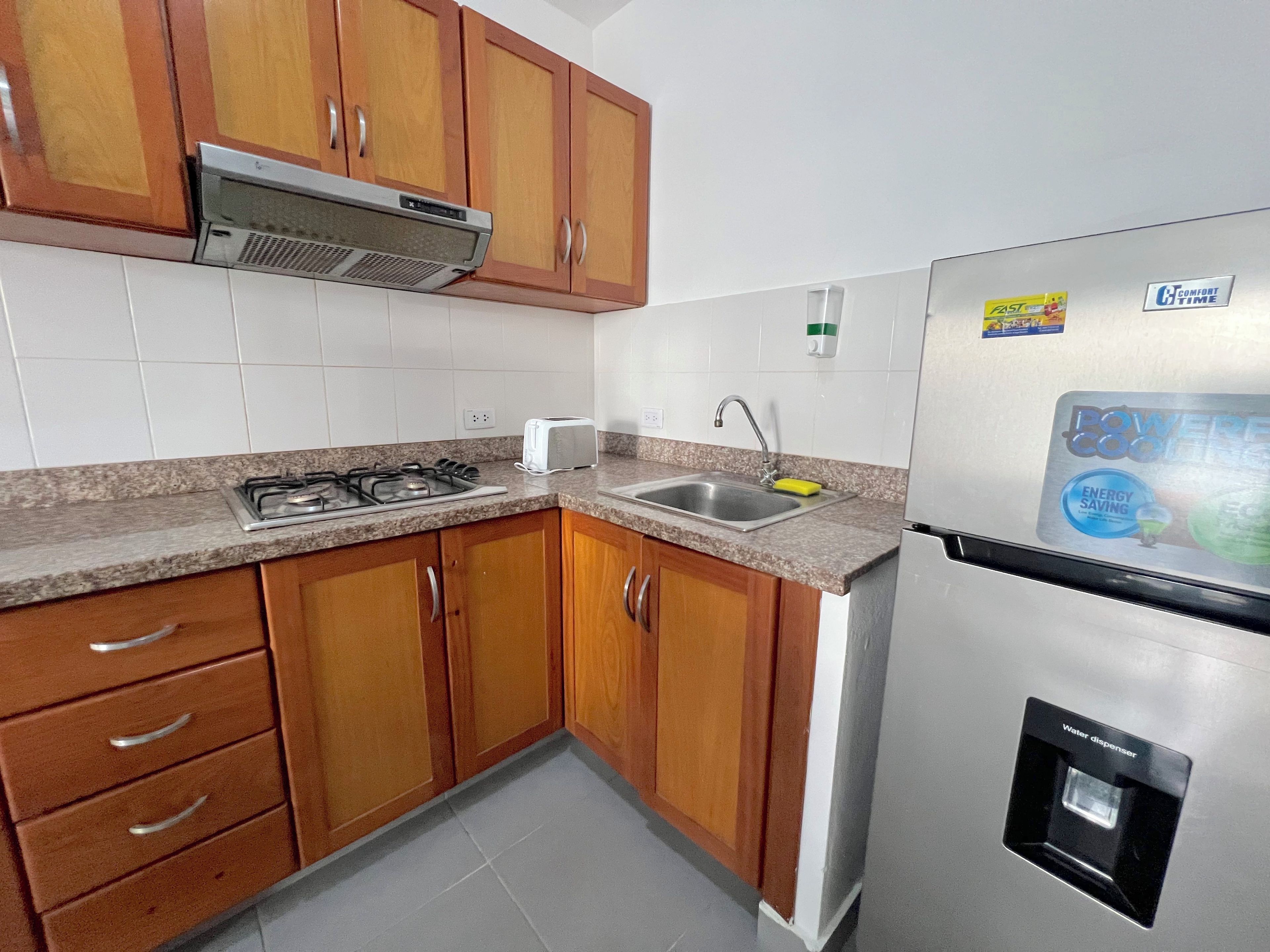A kitchen with wooden cabinets, a stainless steel refrigerator, a gas stove, and a sink.