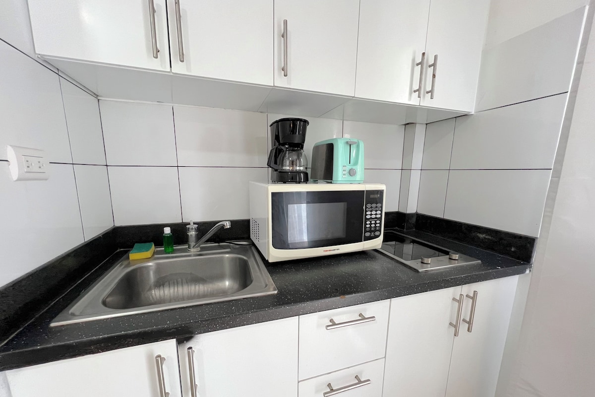 A kitchen with white cabinets, a black countertop, a sink, a microwave, and a coffee maker.