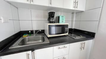 Eine Küche mit weißen Schränken, einer schwarzen Arbeitsplatte, einem Spülbecken, einer Mikrowelle und einer Kaffeemaschine.