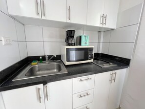 A kitchen with white cabinets, a black countertop, a sink, a microwave, and a coffee maker.