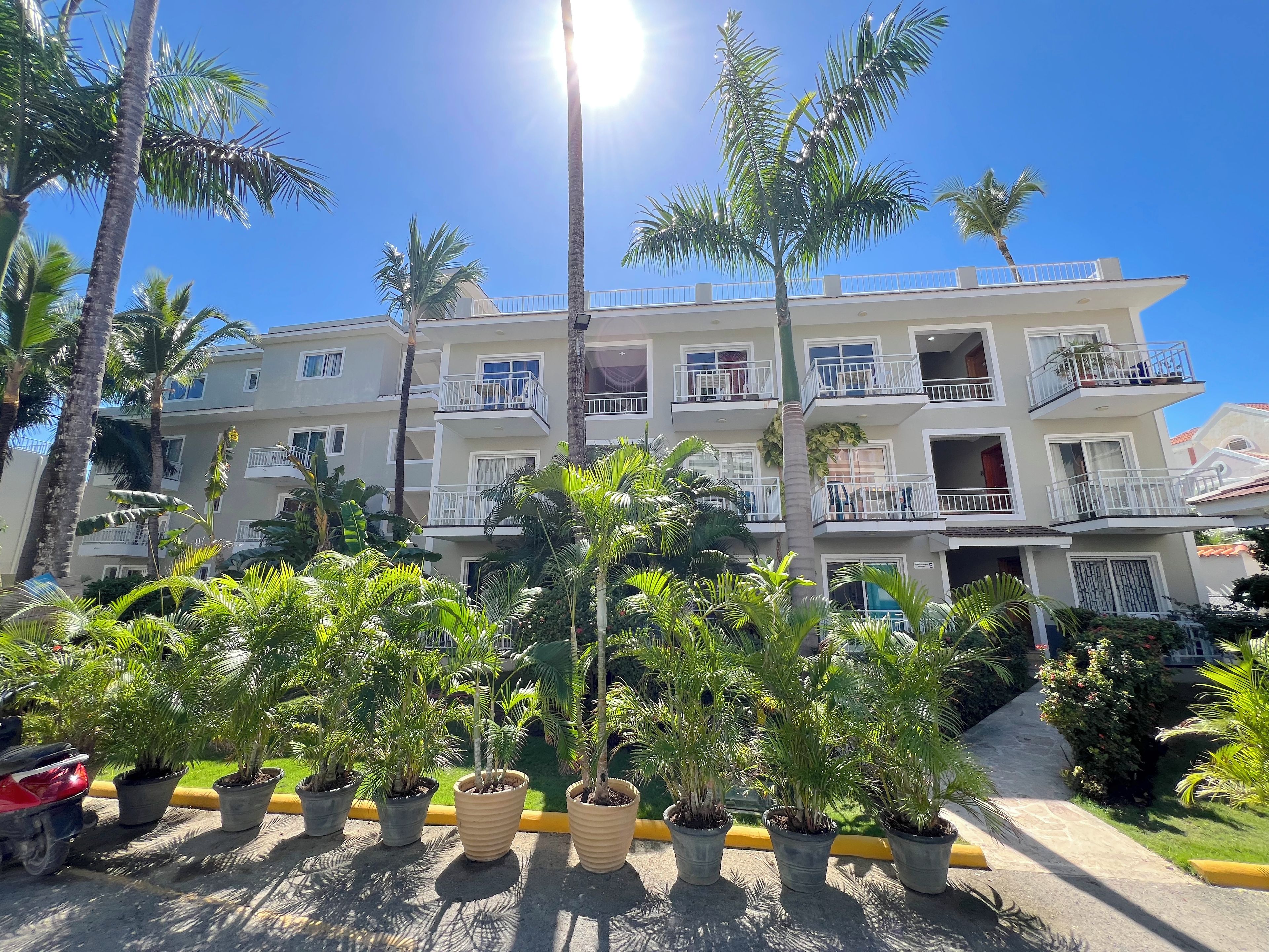 Un hôtel à plusieurs étages, doté de balcons, de plantes en pot et surplombant un ciel d’un bleu limpide.