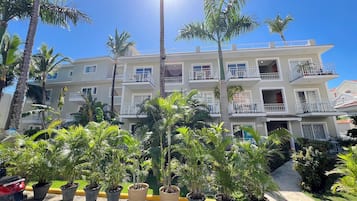 Un hôtel à plusieurs étages, doté de balcons, de plantes en pot et surplombant un ciel d’un bleu limpide.