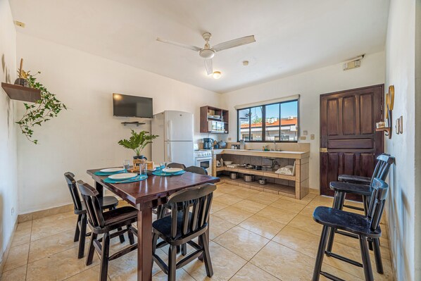 A dining area with a wooden table and chairs, a television mounted on the wall, and a ceiling fan. - Near Beach! Playas del Coco Condo w/ Pool (Playas del Coco)