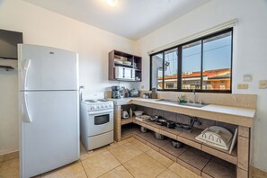 Cozinha compacta com geladeira, fogão e janela com vista para um edifício.
