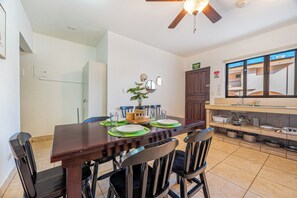 A dining area with a wooden table set for four, chairs, a ceiling fan, and a kitchen area with a sink and countertop visible. - 1 Mi to Beach: Playas del Coco Condo w/ Pool (Playas del Coco)